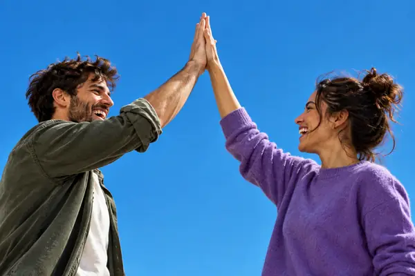 Zwei Creator feiern eine Zusammenarbeit mit einem High-Five vor einem klaren blauen Hintergrund.