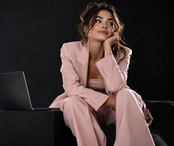 Fashion-Creator in einem hellrosa Outfit posiert vor dunklem Hintergrund bei einem redaktionellen Content-Shooting.